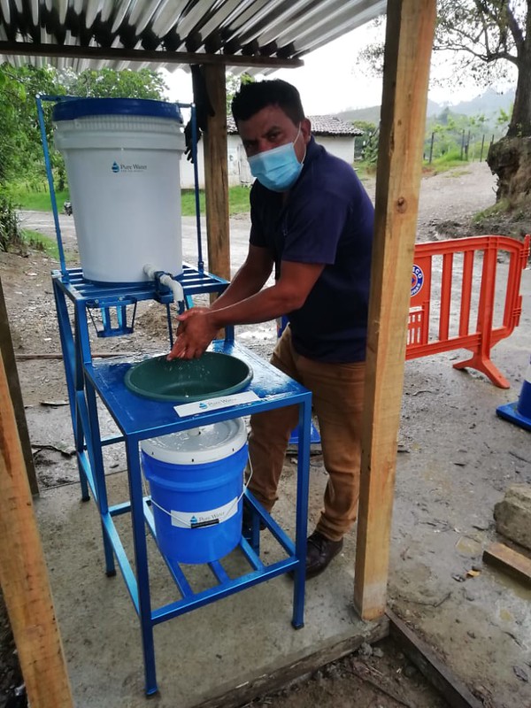 Honduras staff member demoing hands-free wash station of PWW design, inspired by COVID-19.  Photo credit: Pure Water for the World, Inc.