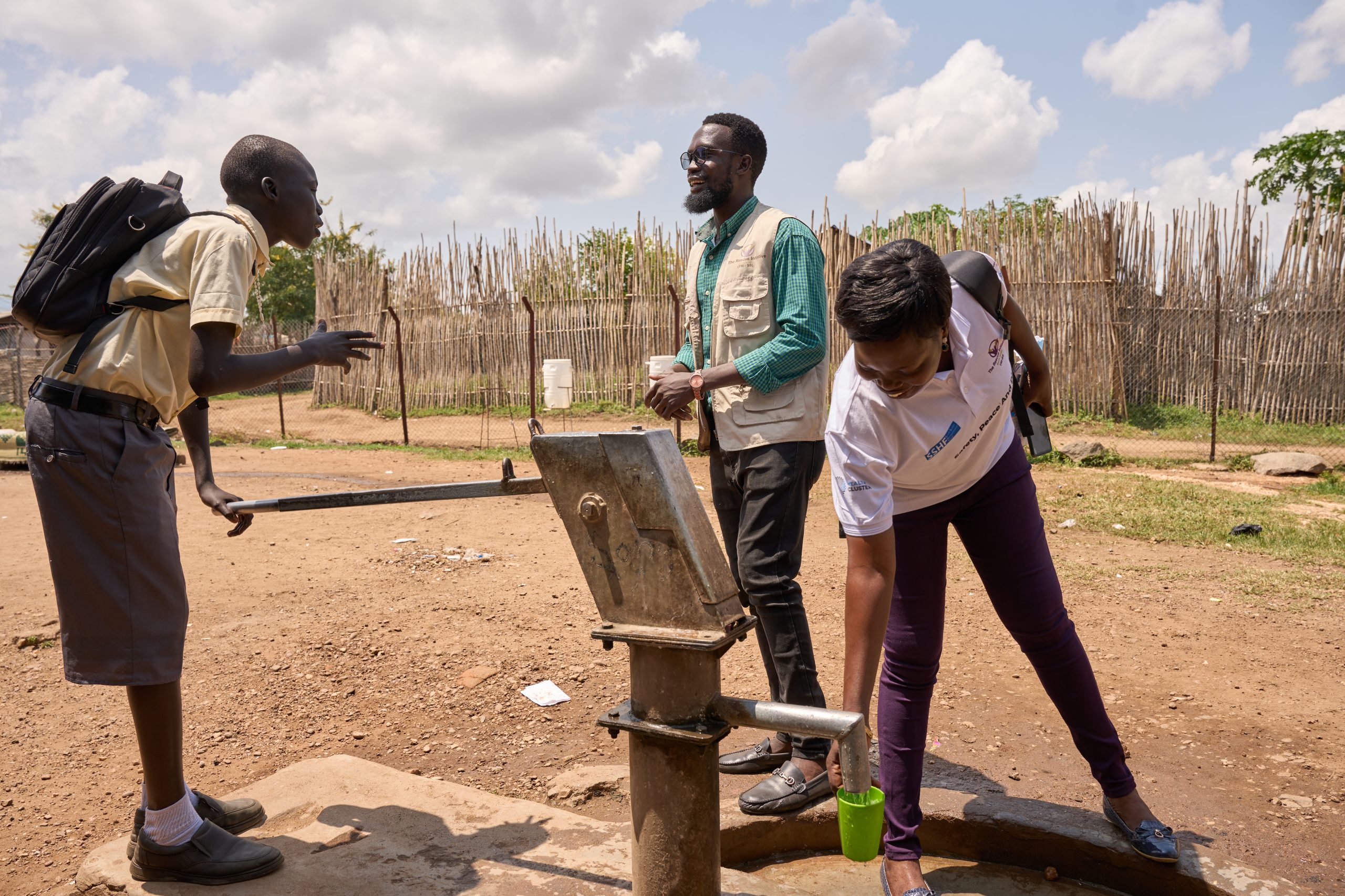 School staff demonstrate the operation of a fresh water pump. A young schoolboy holds the handle of the fresh water pump.
