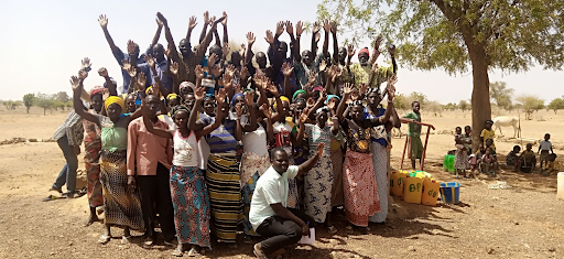 Members of the Water Users Association supported by USAID/TerresEauVie pose for a picture with their hands raised; women are well represented in the group.